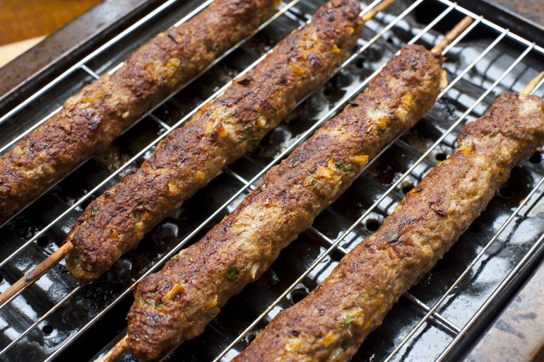 Grilled spicy shish kebabs made with seasoned minced meat, probably lamb, threaded on skewers, lying on an oven grill pan