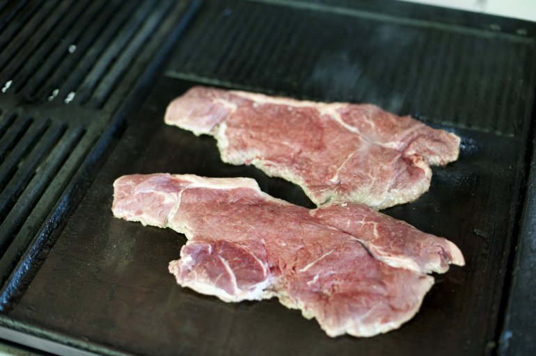 Two lean tender strip steaks cooking over a BBQ griddle viewed high angle