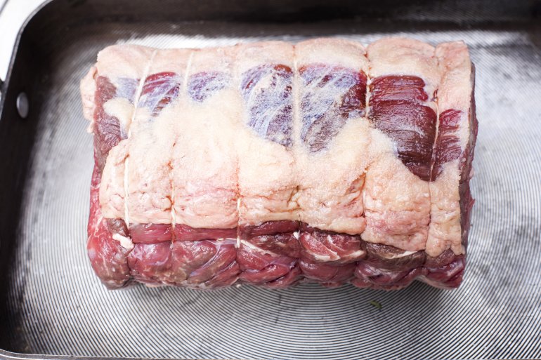Uncooked beef joint ready for roasting in a metal oven pan in a close up high angle view