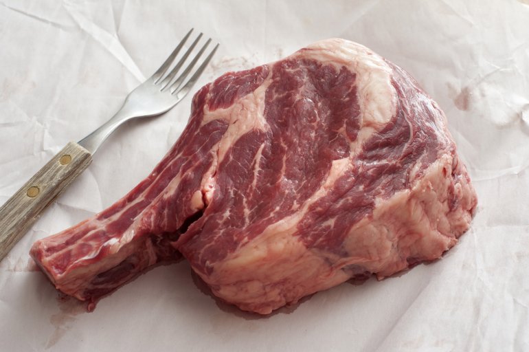 Thick juicy fatty uncooked rib eye beef steak on crumpled white paper with a fork