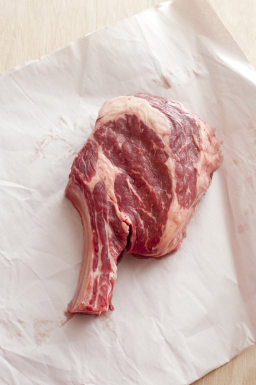 Uncooked thick juicy ribeye steak on crumpled white paper viewed from overhead in vertical format