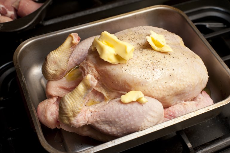 Uncooked seasoned chicken with dollops of butter on top lying in a roasting pan ready to go into the oven for roasting
