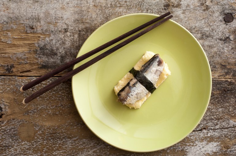 Top down view of fish and egg omelet square in plate with chopsticks over weathered wooden table