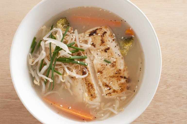 Asian fish soup with portions of grilled fish steaks in a savory broth with noodles, carrots and chives viewed from overhead