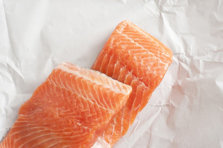 Close up top down view on stack of two fresh raw salmon slices in unwrapped white butcher paper with copy space