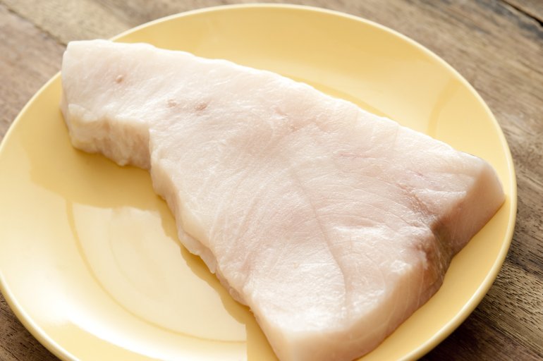 Top down close up view on single Triangle shaped piece of raw swordfish meat in the middle of round yellow china plate