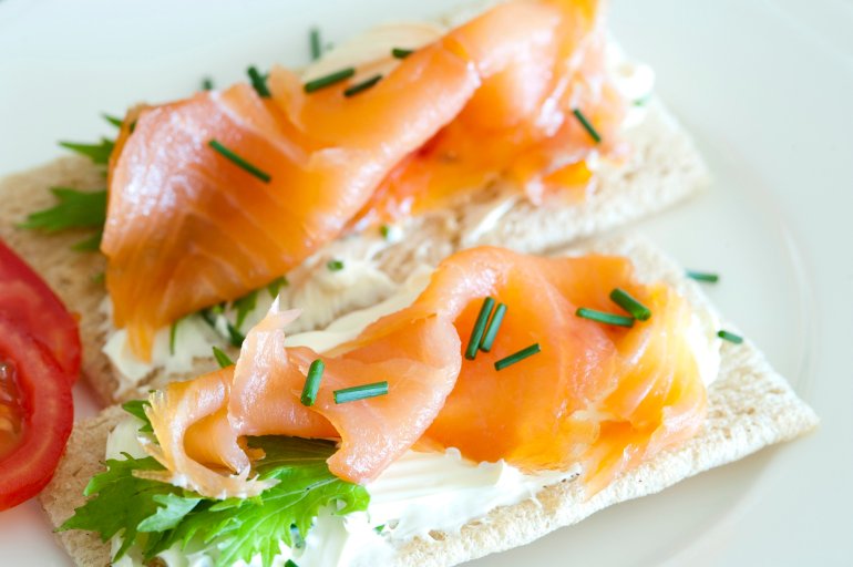Gourmet lunchtime snack of thinly sliced cured and smoked marine salmon on crispbread with fresh lettuce and chives