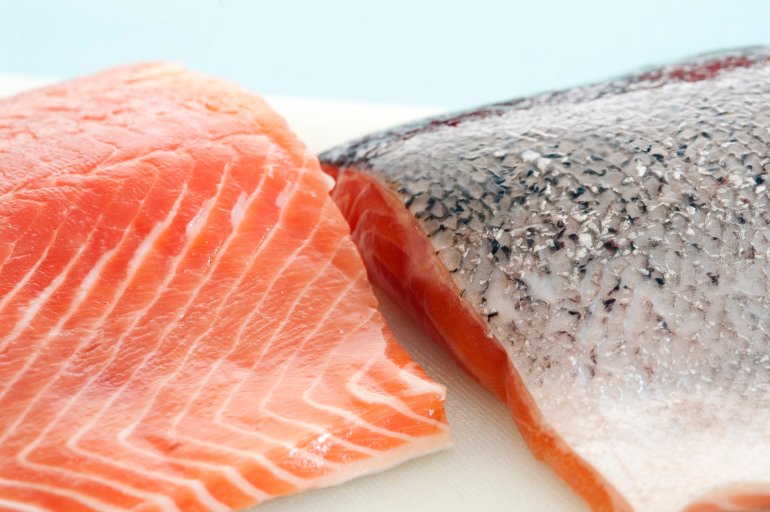 Two fresh raw salmon fillets, one with the flesh exposed and one showing the skin texture while preparing a gourmet seafood meal