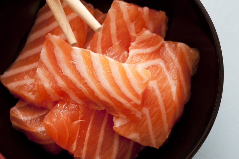 First person perspective view from top down over sashimi raw fish strips with chopsticks close up