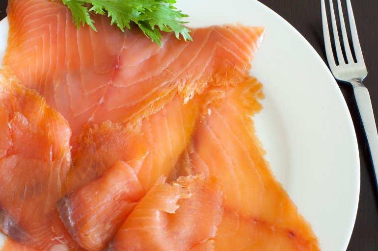 Fresh cured and smoked salmon slices served on a plate for a gourmet seafood dinner, close up overhead view