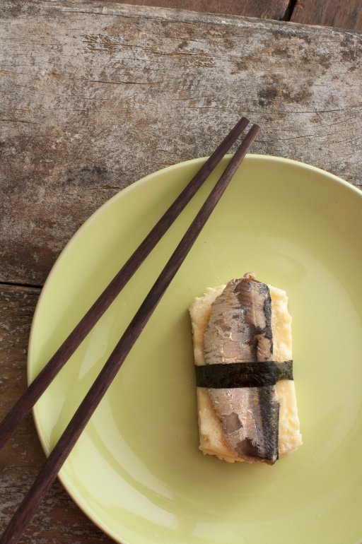 Top down view of single serving of wrapped mamagoyaki sardine with brown chopsticks and round green plate
