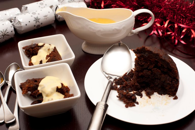 Delicious fruity Christmas pudding with brandy cream sauce served in dishes on a decorative Christmas table for a seasonal Xmas celebration