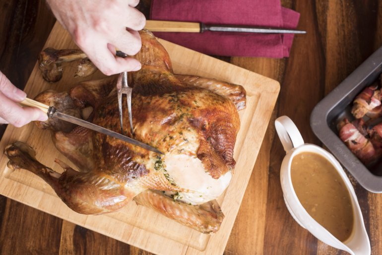 Person carving roasted thanksgiving turkey on wooden board