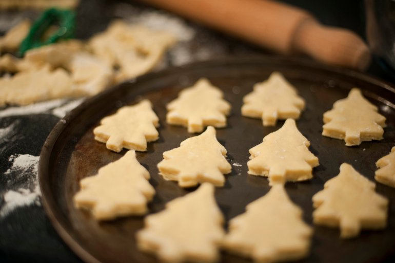 Metal baking tray arranged with homemade pastry in the shape of Christmas tree cookies during the preparation and baking of the delicious traditional biscuits