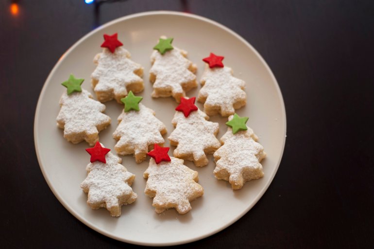 Plate of freshly baked homemade Christmas tree cookies decorated with colourful stars in green and red, high angle view