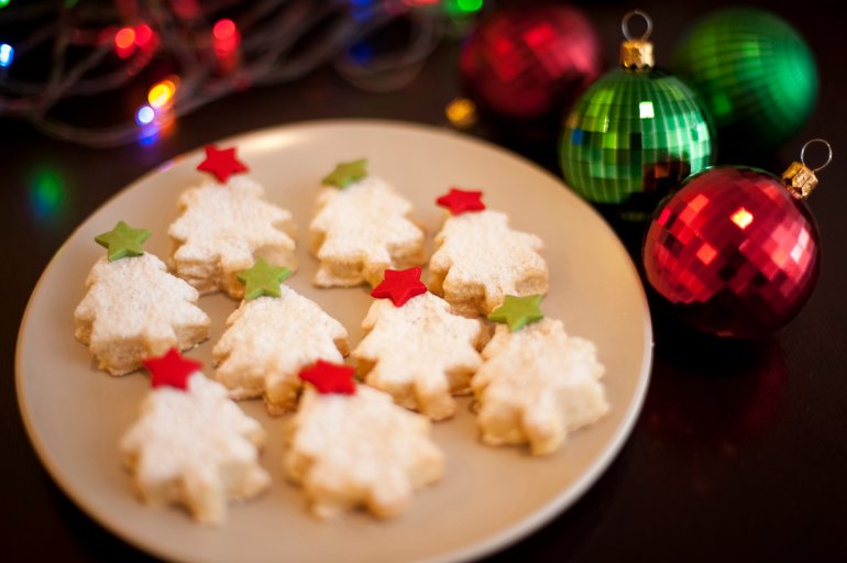 Golden freshly baked Christmas cookies in the form of Christmas trees decorated with colourful, red and green stars served on a plate, high angle view with Xmas ornaments