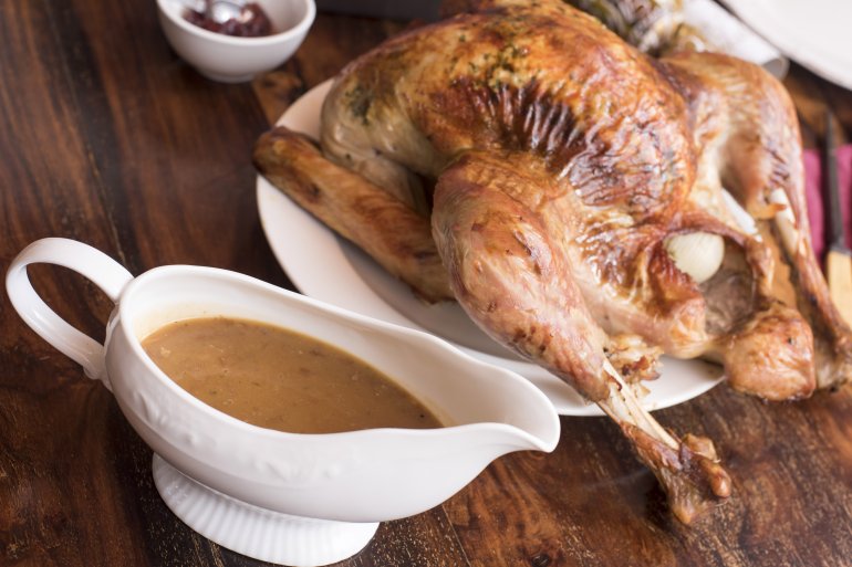 Crispy roasted whole turkey with gravy in a sauce boat for Christmas or Thanksgiving