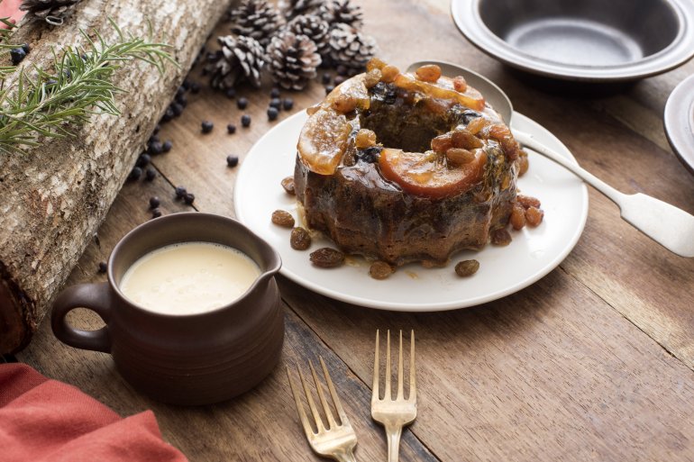 Small plum pudding with brandy custard or sauce ready to be served for Christmas dessert on a decorated wooden table