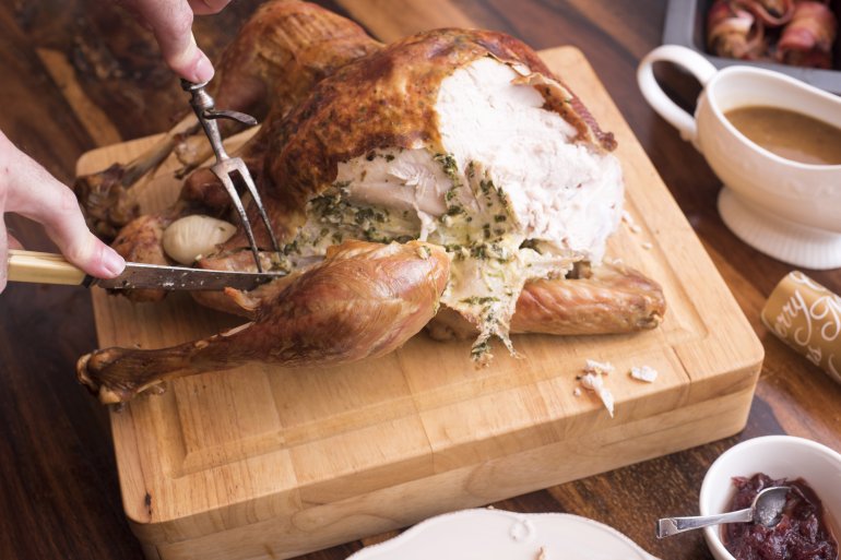 Man carving a roast turkey for Christmas dinner on a wooden cutting board on a festive table laid with all the trimmings