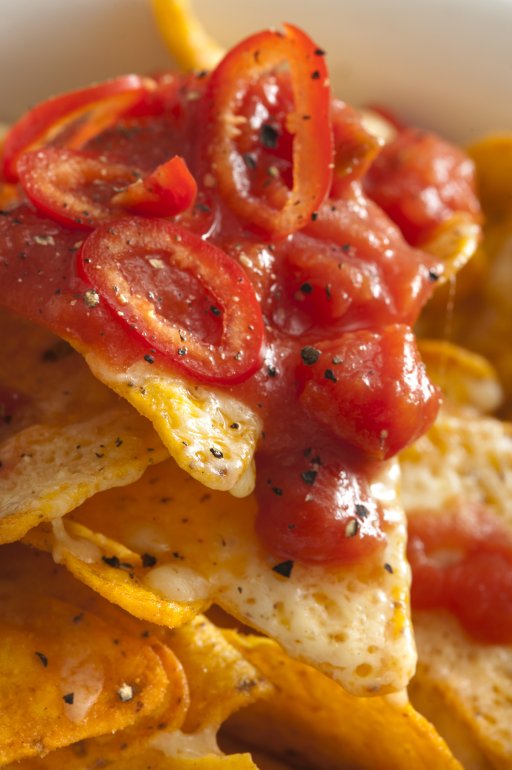 Topping of hot chili pepper and tomato salsa on corn tortilla chips with melted cheese for a tasty Tex-Mex or Mexican snack