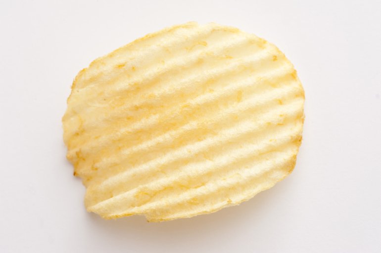 Single crinkle cut potato crisp or chip on a white background viewed close up from above