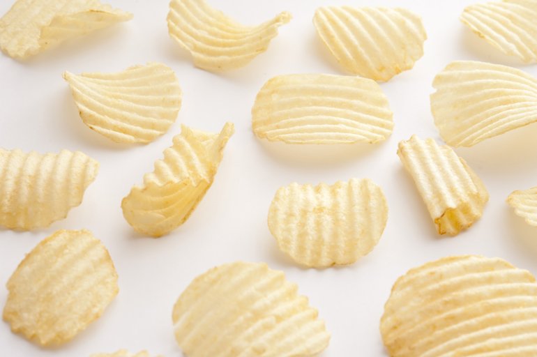 First person perspective view on individual ridged yellow crispy potato chips over white background