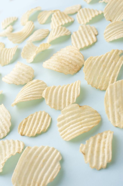 Background of scattered crinkle cut potato crisps on a light green background viewed high angle for a tasty but unhealthy snack