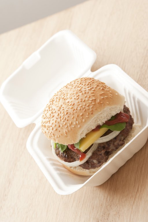 First person angled view on freshly prepared hamburger filled with onions, ketchup, cheese and lettuce in take out carton