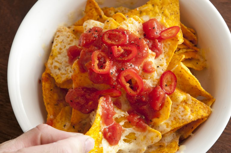 Man eating nachos and chili peppers topped with melted cheese for a traditional Mexican snack or appetizer