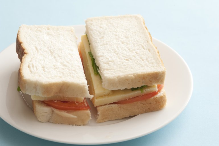 A plain boring bread sandwich with a filling of tomato and sliced cheese sliced through the centre on a plate in a close up view