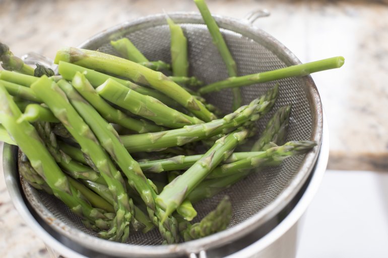 Blanched fresh seasonal green asparagus spears draining in a metal sieve in the kitchen