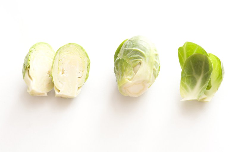 Whole and halved fresh Brussel sprouts with loose leaves arranged in a row on white with copy space