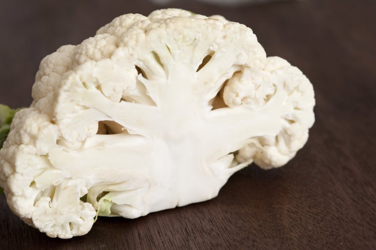Halved fresh white head of a cauliflower on a dark wooden table with focus to the cross-section