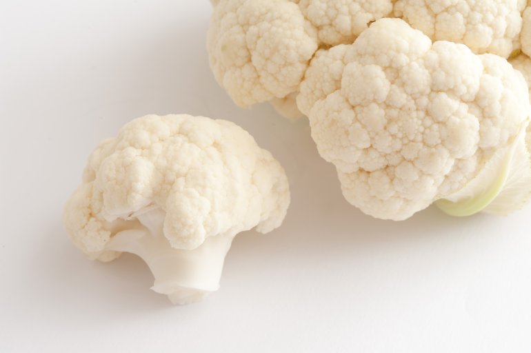 Focus to a single floret of fresh uncooked white cauliflower with additional florets alongside ready for cooking as a tasty healthy vegetable accompaniment