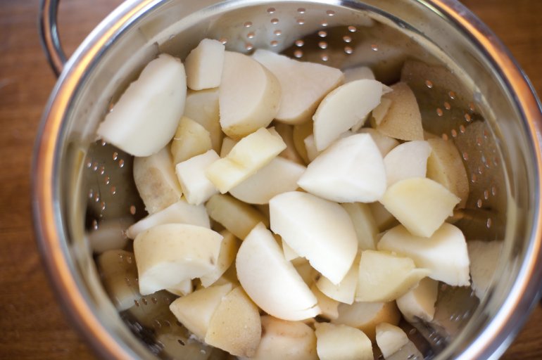 Chopped white potatoes in colander viewed from above in close-up