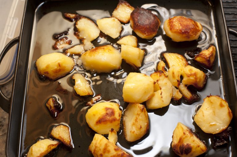 Crispy golden roast potatoes in an oily grill pan waiting to be served for dinner, close up high angle view