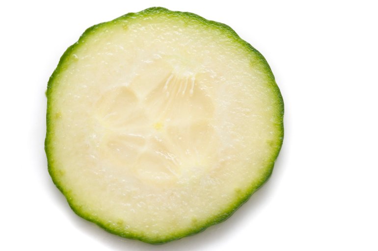 Single thin slice of fresh cucumber prepared for a salad showing the texture of the juicy fleshy pulp, pips and rind on white