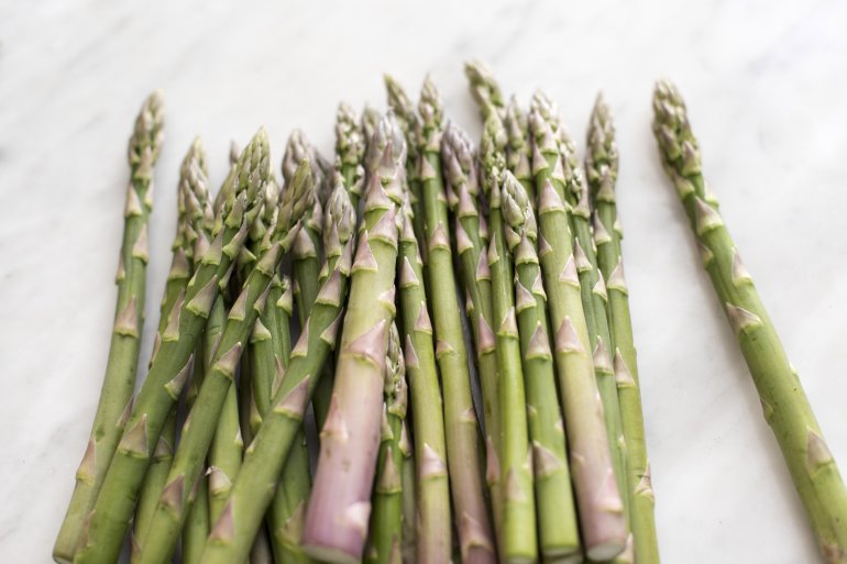 Pile of fresh raw seasonal green spring asparagus tips, shoots or spears on a white background