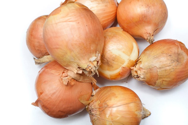 Pile of fresh whole raw brown onions, a pungent aromatic vegetable used in cooking as a flavouring