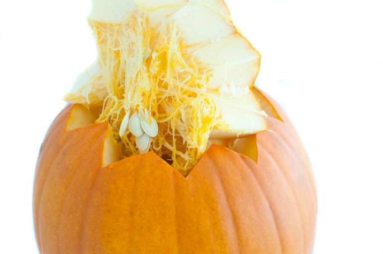 Decoratively cut fresh pumpkin with the cut portion lifted away to reveal the fibres and healthy pips inside over a white background