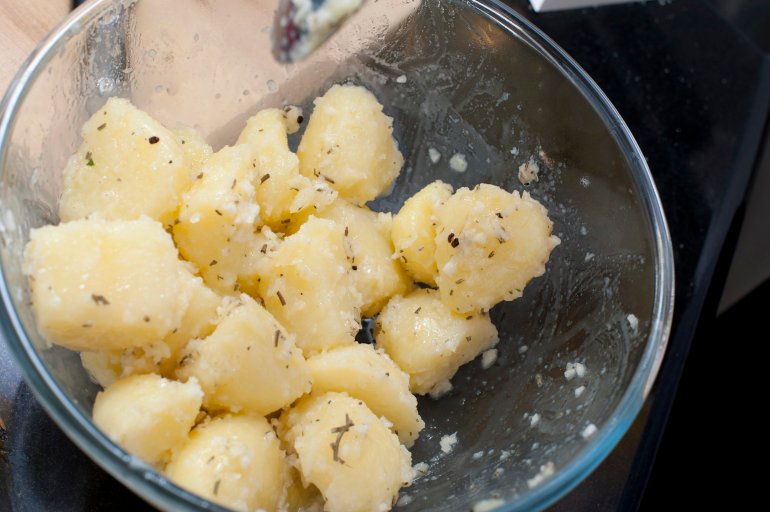 Seasoned peeled diced boiled potatoes in a glass bowl during preparation of a meal in the kitchen
