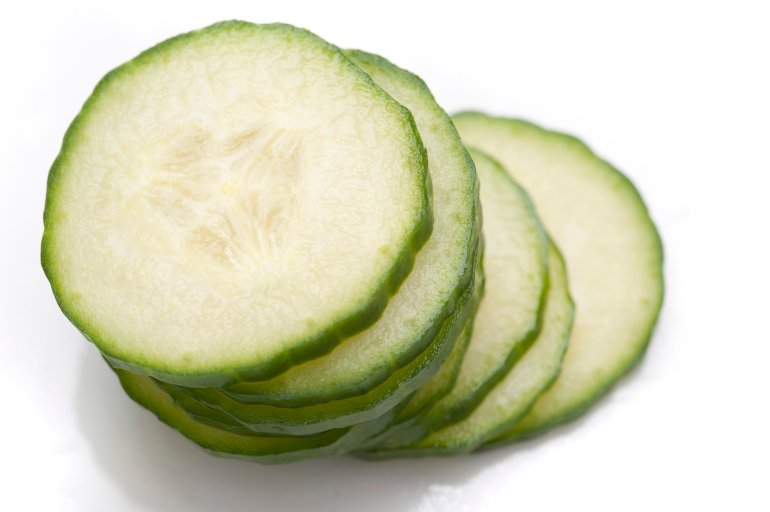 Stack of thin cucumber slices with focus to the top slice showing texture detail of the succulent flesh and pips