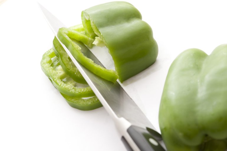 Close-up of green pepper cut in slices with knife. White background