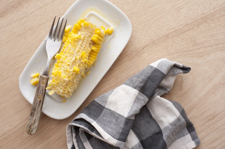 Eaten corn cob on white plate with fork and checked napkin. From above