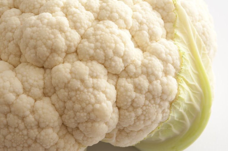 Close up view of the florets and texture of a head of fresh white cauliflower over a white background